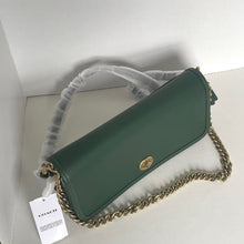 Load image into Gallery viewer, Green handbag with gold chain strap on a white surface, featuring a Coach tag.