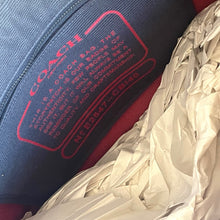 Load image into Gallery viewer, Close-up of a Coach bag label with red text on a blue background, partially covered by crumpled white paper.