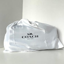 Load image into Gallery viewer, Coach bag wrapped in a satin cover on a light gray background