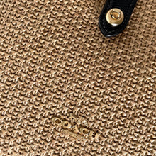 Load image into Gallery viewer, Close-up of a textured beige surface with a gold logo and black strap.