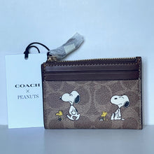 Load image into Gallery viewer, Coach x Peanuts wallet with Snoopy and Woodstock designs on a light blue background