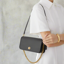 Load image into Gallery viewer, Person holding a black handbag with a gold chain strap on a white background