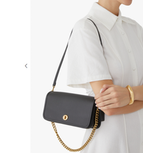 Load image into Gallery viewer, Person holding a black handbag with a gold chain strap against a white background