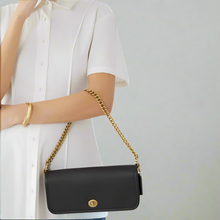 Load image into Gallery viewer, Black handbag with gold chain strap held by a person wearing a white shirt.