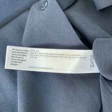Load image into Gallery viewer, Close-up of a label on a piece of gray fabric with text.