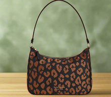 Load image into Gallery viewer, A small black leopard print nylon shoulder bag with a Kate Spade logo, displayed against a pink background with green foliage.