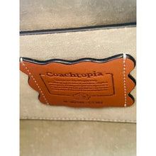 Load image into Gallery viewer, Close-up of a Coachtopia branded leather tag on a beige background