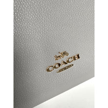 Load image into Gallery viewer, Close-up of a Coach logo on a textured gray surface