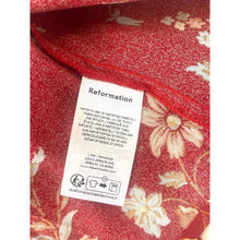 Load image into Gallery viewer, Red fabric with floral patterns and a visible 'Reformation' label.