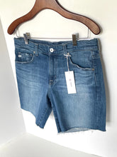 Load image into Gallery viewer, Blue denim shorts on a hanger with a tag against a white background