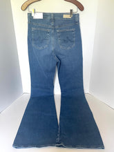 Load image into Gallery viewer, Blue denim flare jeans hanging on a wooden hanger against a white background, showing the back pockets and flared leg.