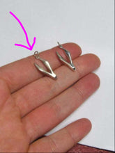Load image into Gallery viewer, A pair of small silver dangling earrings with a unique curved, wing-like shape, shown resting on an open hand against a plain white background.