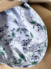 Load image into Gallery viewer, Close-up of a fabric-covered circular product, likely a cup or pad, featuring a white satin-like surface with a delicate floral print in green and navy blue, resting on a tan textured background.