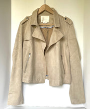 Load image into Gallery viewer, A light beige suede moto jacket hanging on a wooden hanger against a plain white wall.