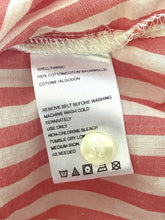 Load image into Gallery viewer, Close-up of a white garment care label sewn onto red and white striped fabric, showing washing instructions and a small gold button.