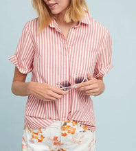Load image into Gallery viewer, A woman wearing a pink and white vertically striped short-sleeve button-up shirt and white floral shorts, holding a pair of sunglasses against a light blue background.