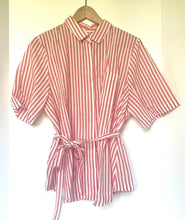 Load image into Gallery viewer, A short-sleeve collared shirt dress with vertical pink and white stripes, featuring a tie waist belt, hanging on a wooden hanger against a plain white background.