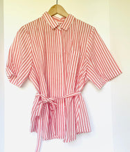 Load image into Gallery viewer, A pink and white vertically striped short-sleeve collared shirt dress with a self-tie belt, hanging on a wooden hanger against a white background.