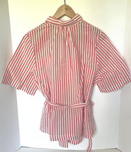 Load image into Gallery viewer, A short-sleeve collared shirt with vertical red and white stripes, tied at the waist with a matching belt, hanging on a wooden hanger against a white background.