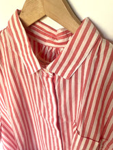Load image into Gallery viewer, A red and white vertically striped button-down shirt with a pointed collar, hanging on a wooden hanger against a plain off-white wall.