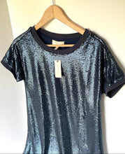 Load image into Gallery viewer, A short-sleeve crewneck t-shirt with a shimmering metallic blue-gray sequin texture, hanging on a wooden hanger against a plain off-white wall.