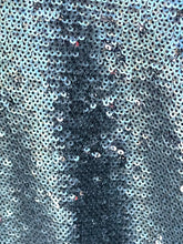 Load image into Gallery viewer, A close-up of a shimmering sequin fabric with a metallic silver and light blue color identity, featuring a central vertical area with darker, denser sequins.