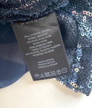 Load image into Gallery viewer, A close-up of a black sewn-in care label attached to a dark navy blue sequined garment, with a soft cream-colored fabric background.