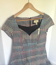 Load image into Gallery viewer, A vintage plaid dress with short sleeves and a black V-neckline, hanging on a wooden hanger against a plain off-white wall.