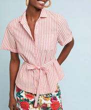 Load image into Gallery viewer, A woman wearing a short-sleeve collared button-front shirt with pink and white vertical stripes and a matching tie belt at the waist, paired with a colorful floral skirt against a light blue background.