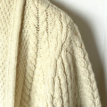 Load image into Gallery viewer, Close-up of a cream-colored knitted sweater with cable pattern.