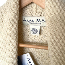 Load image into Gallery viewer, Close-up of a beige knitted sweater with 'Aran Mór' label showing 100% Merino Wool.