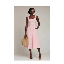 Load image into Gallery viewer, Woman wearing a pink dress holding a straw bag against a neutral background