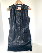 Load image into Gallery viewer, A sleeveless black faux-leather dress with a quilted patchwork pattern, button-front closure, and front pockets, hanging on a wooden hanger against a white wall.