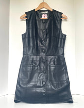 Load image into Gallery viewer, A black faux leather sleeveless dress with a quilted pattern, button-down front, and large front pockets, hanging on a wooden hanger against a white wall.