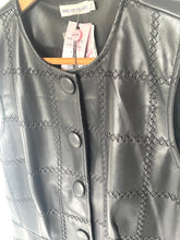 Load image into Gallery viewer, A black faux-leather vest with a diamond grid pattern and decorative stitching, featuring a button-up front. The vest is shown hanging on a wooden hanger with tags attached, including a tag that reads 'AVEC LES FILLES'.
