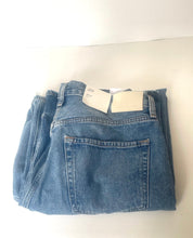 Load image into Gallery viewer, A pair of folded blue denim jeans with a paper price tag attached at the waistband, displayed on a plain white surface.