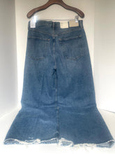 Load image into Gallery viewer, A pair of medium-wash blue denim skirt jeans with a wide flared leg and raw frayed hem, hanging on a wooden hanger against a plain white wall.