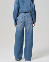 Load image into Gallery viewer, A person shown from the back wearing wide-leg blue denim jeans and a matching blue denim long-sleeve top against a plain light gray studio background.