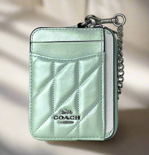Mint green quilted Coach wallet with keychain on a light gray surface.