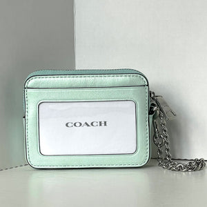 Mint green Coach wallet with chain strap on a light gray background