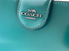 Load image into Gallery viewer, Close-up of a Coach logo on a teal background