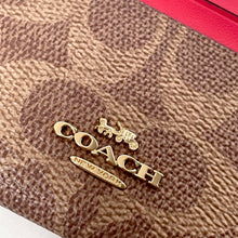 Load image into Gallery viewer, Close-up of a Coach logo on a textured brown surface with a pink item partially visible.
