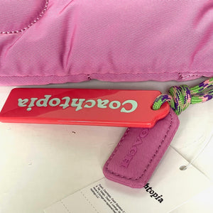 Pink Coach bag with a red tag on a white surface