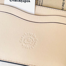 Load image into Gallery viewer, Close-up of a beige leather product with 'Coachtopia' branding.