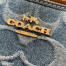 Load image into Gallery viewer, Gold 'Coach' logo with a horse and carriage on denim fabric