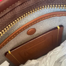Load image into Gallery viewer, Close-up of a brown leather wallet with gold stitching inside a textured bag.
