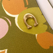 Load image into Gallery viewer, Gold earring on a colorful patterned surface