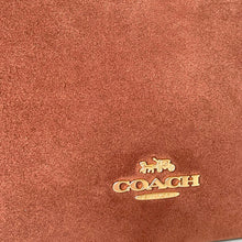 Load image into Gallery viewer, Close-up of a Coach logo on brown leather