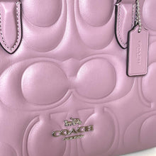 Load image into Gallery viewer, Close-up of a pink Coach handbag with embossed logo and visible brand tag.
