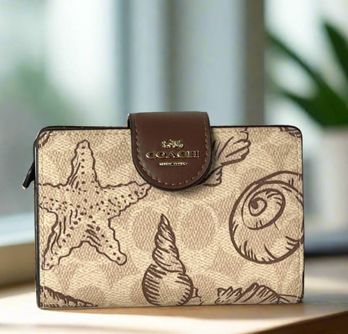 Coach wallet with shell design and brown leather flap on a white background